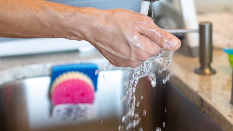 Une personne fait couleur de l'eau du robinet avec sa main en-dessous